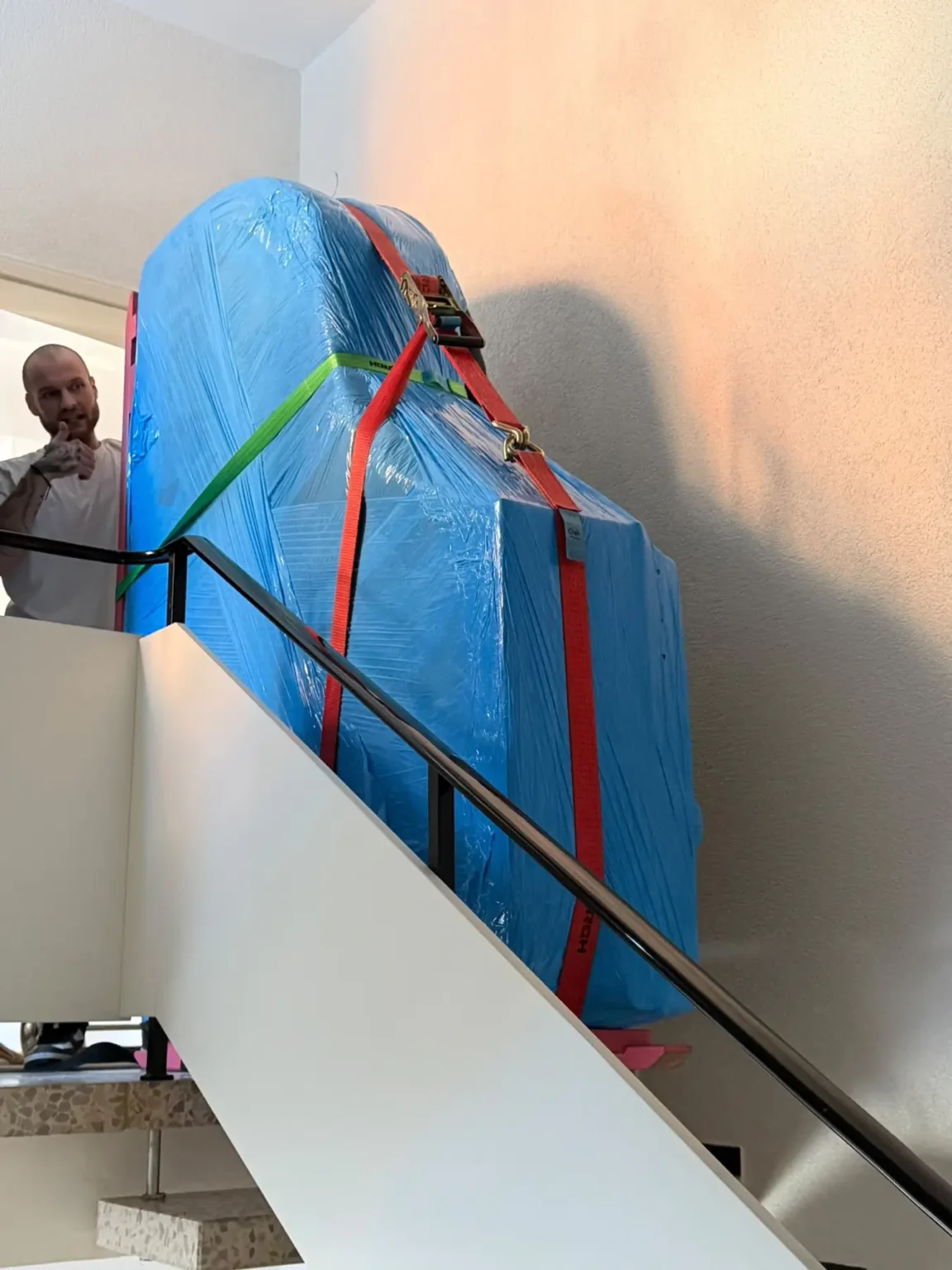 Ein in Schutzfolie verpackter Flügel wird auf dem Flügelbrett über ein Treppenhaus nach oben bewegt