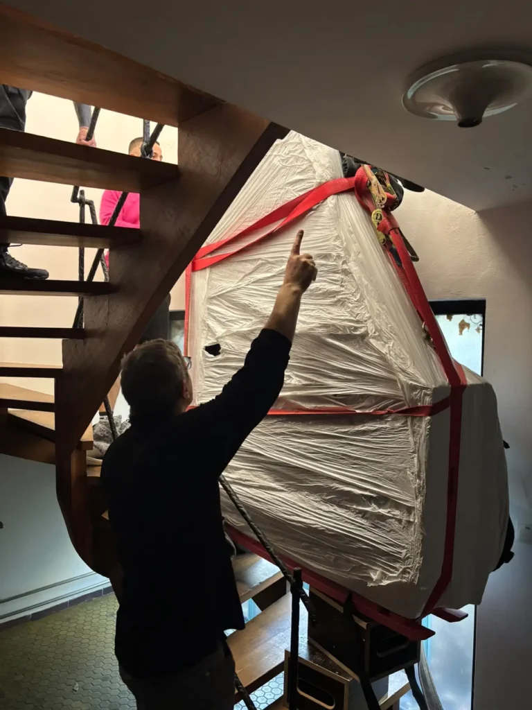 Ein verpackter Flügel wird mit dem Pianoplan über eine offene Holztreppe nach oben bewegt