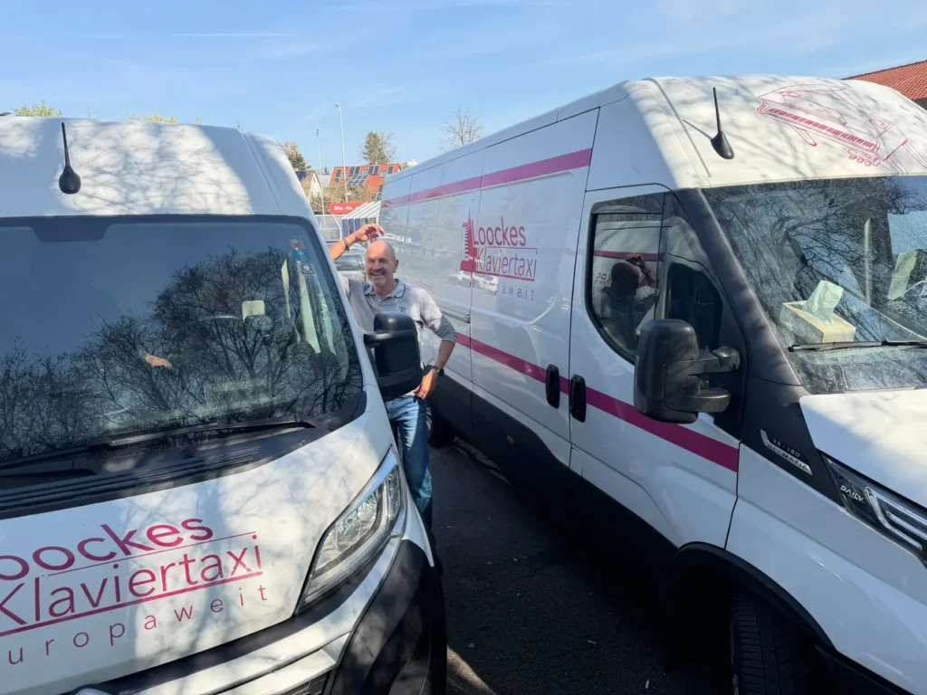 Zwei beschriftete Transporter von Loocke's Klaviertaxi nebeneinander auf dem Hof