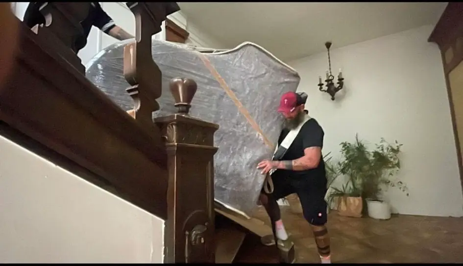 Ein gepolstertes Klavier wird kontrolliert eine Treppe hinuntergetragen