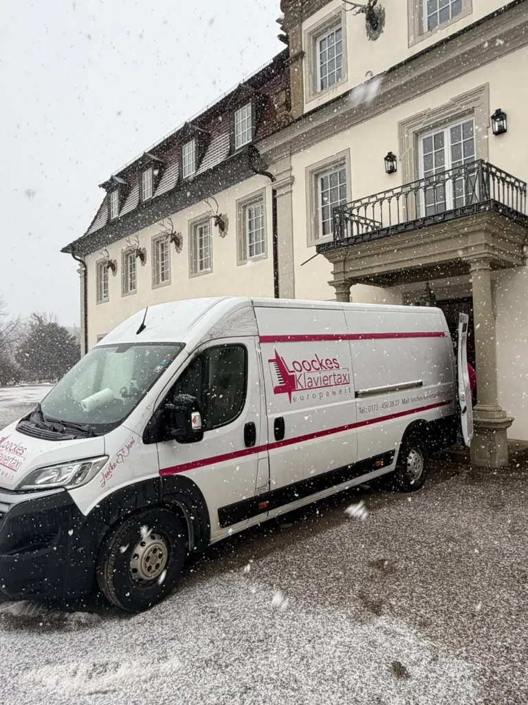 Transporter von Loocke's Klaviertaxi bei Schneefall vor einem historischen Veranstaltungsgebäude